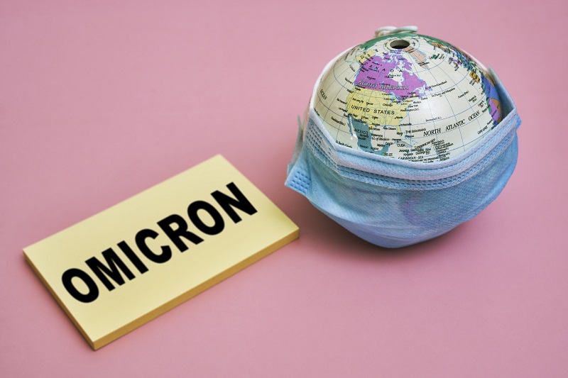 Miniaturowy globus owinięty w maskę, z doczepioną plakietką "Omicron"